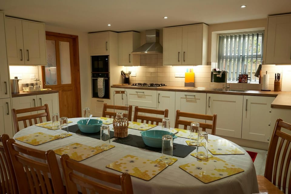 Kitchen in the background with dining table and chairs laid for a meal
