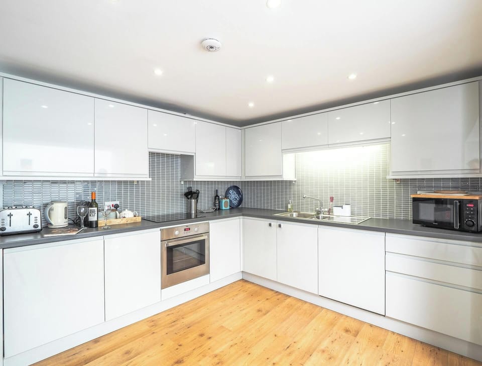 White gloss wall and base cupboards, built-in oven and hob, toaster, kettle and microwave. Tiled splashback