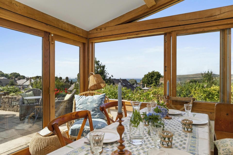 Dining table set with glasses and candles in a sunroom with large wooden-framed windows