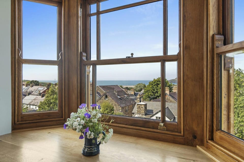 Vase of mixed flowers on a windowsill beside a wooden-framed bay window with sea view