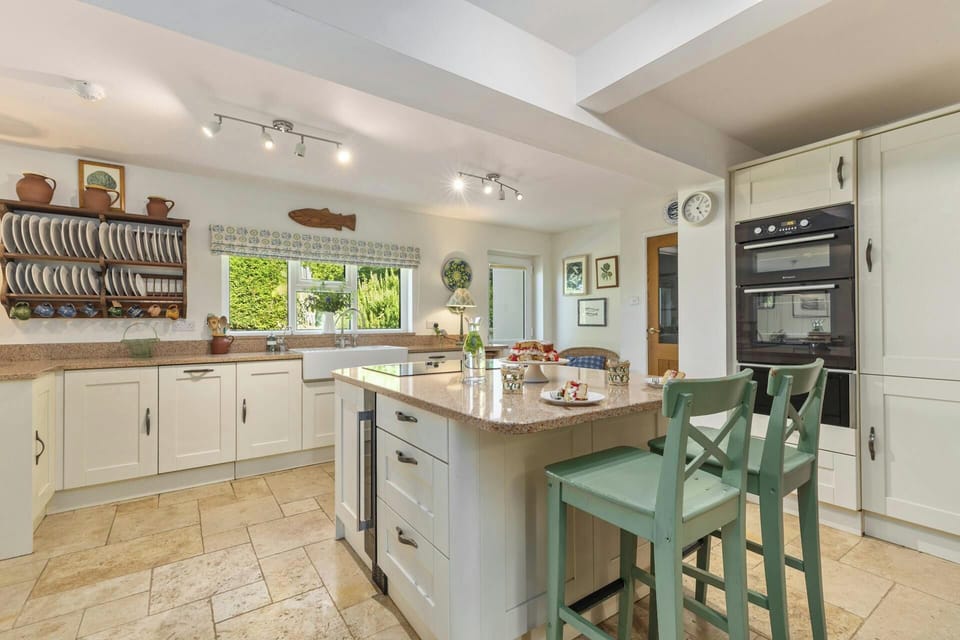 Bright kitchen with central island, two green chairs and stone floor tiles