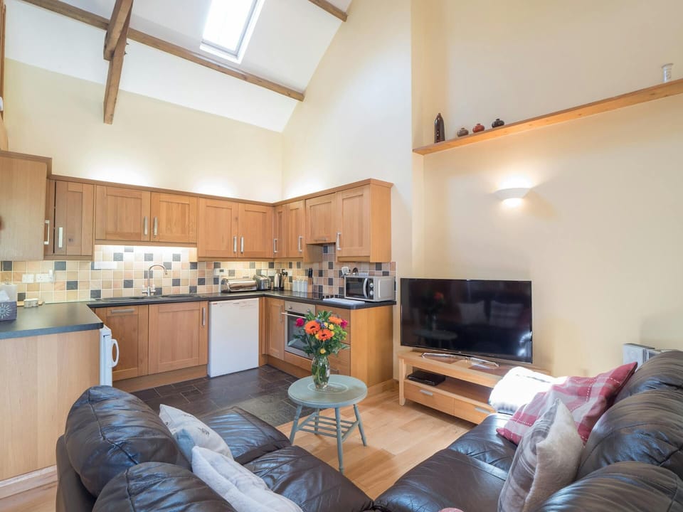 Open plan kitchen and sitting area in Eirlys, fitted units, leather corner sofa, TV and coffee table