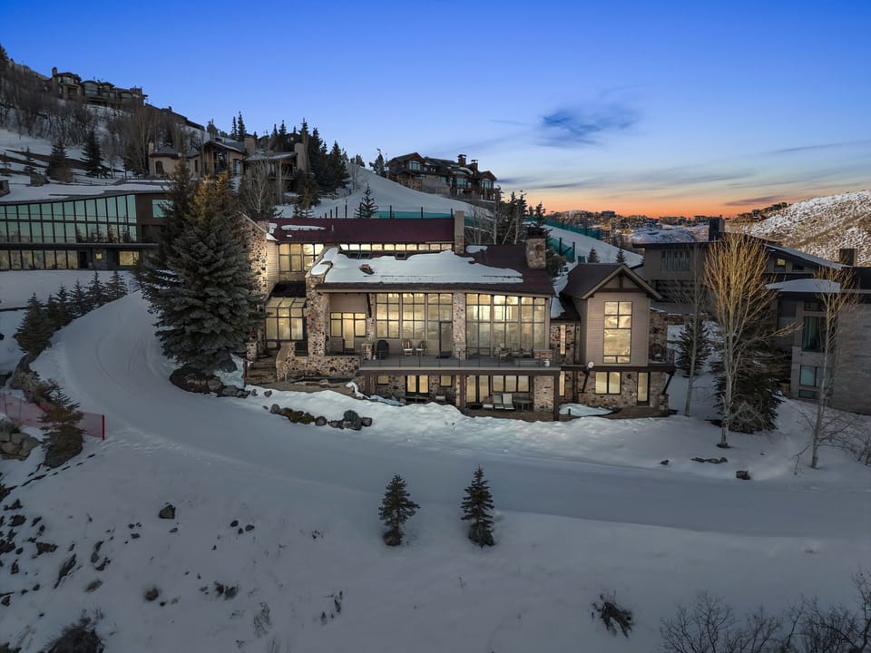 Luxury mountain home exterior at dusk with snow-covered slopes in Park City.