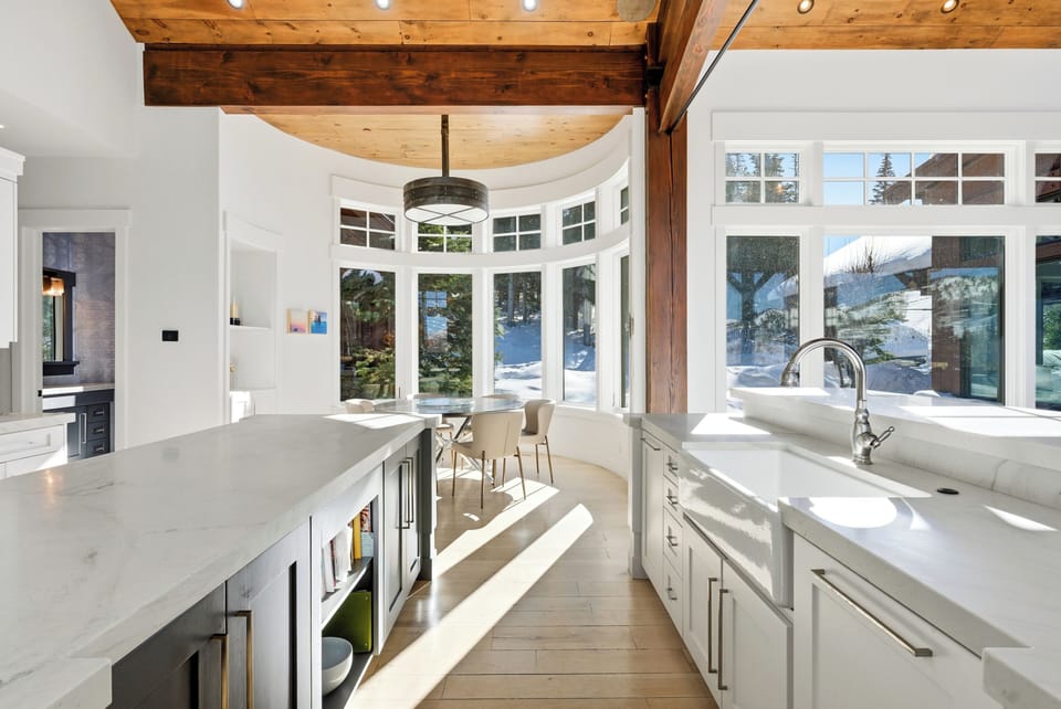 Bright kitchen workspace with long counters:
Elegant kitchen with extended quartz countertops, white cabinetry, and expansive windows offering forest views.