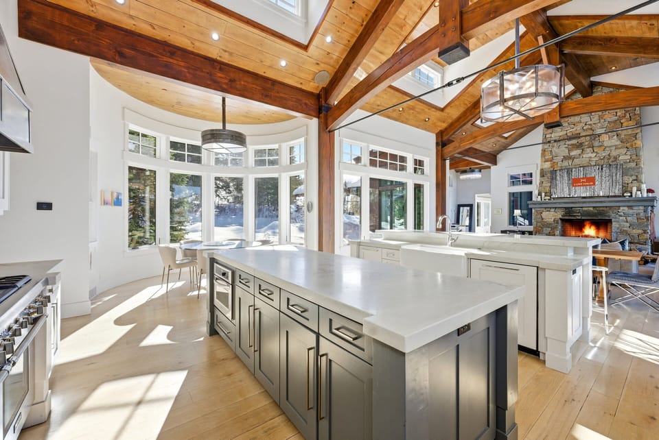 Gourmet kitchen with large island and vaulted ceilings:
Spacious chef's kitchen featuring a large central island, white cabinetry, stainless steel appliances, and vaulted wood-beam ceilings filled with natural light.