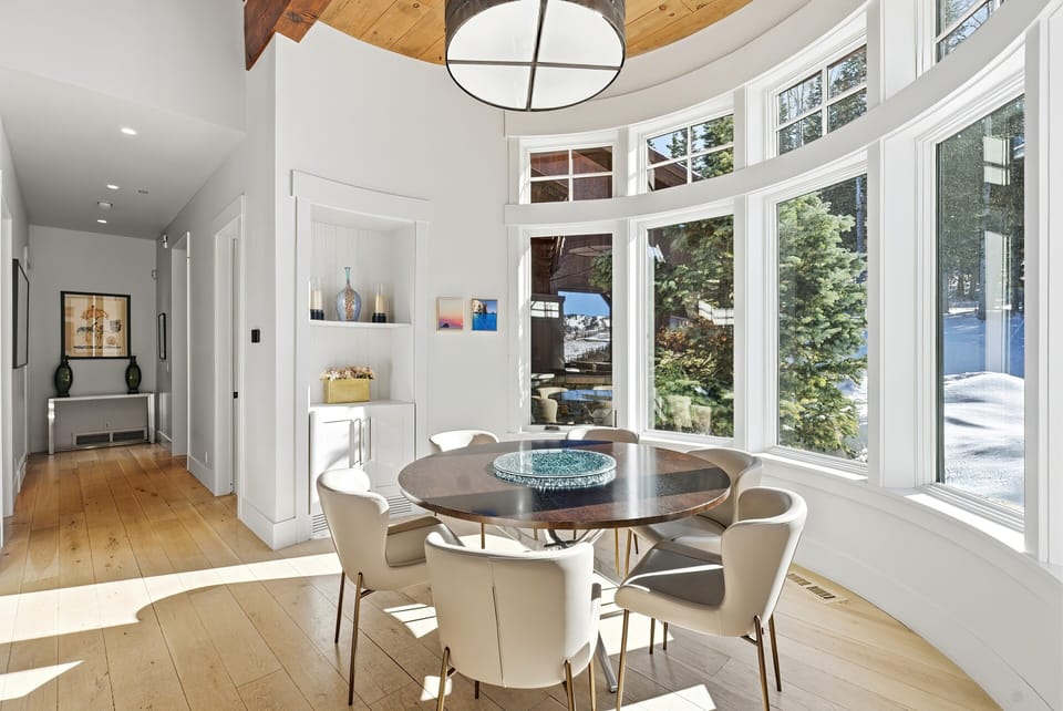 Breakfast nook adjacent to kitchen:
Cozy breakfast nook with a round table, modern chairs, and floor-to-ceiling windows bringing in natural light and outdoor views.
