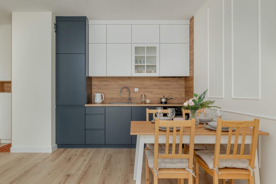 A modern kitchen with dark gray lower cabinets and white upper cabinets, featuring a small wooden dining table. The clean lines and minimalist design offer a sleek, contemporary feel.