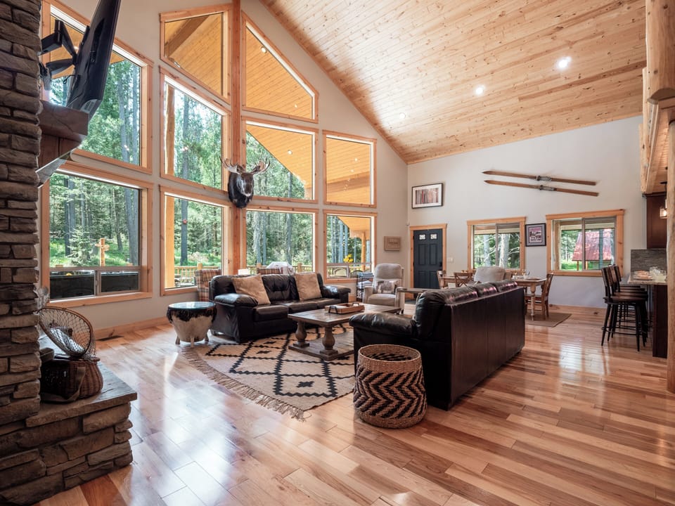 This spacious lodge-style living room is filled with natural light thanks to floor-to-ceiling windows. It offers stunning views of the pines and is the perfect spot to relax comfortably.