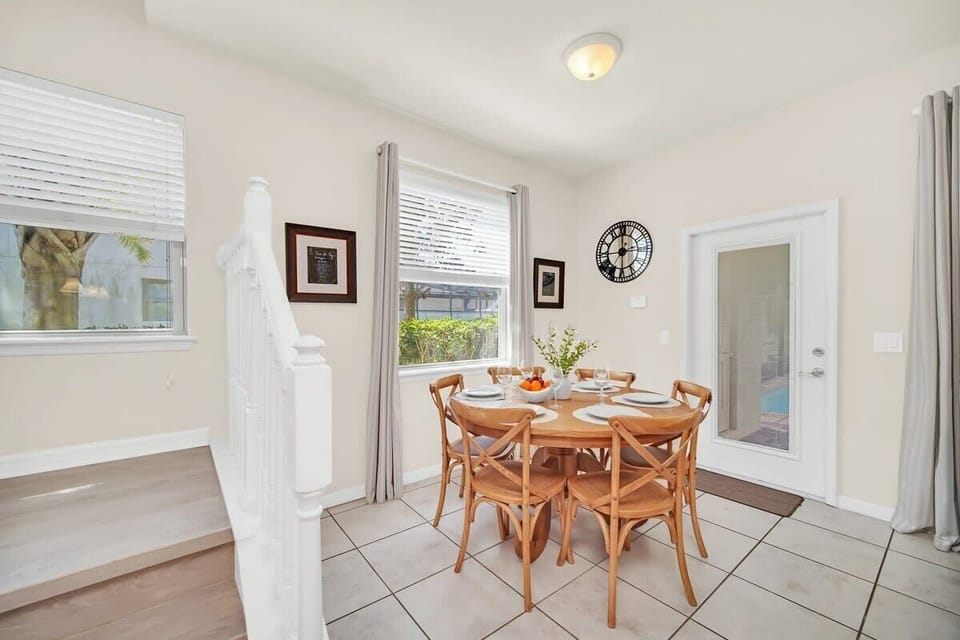 Bright dining area with a wooden table set for six and natural light from two windows.