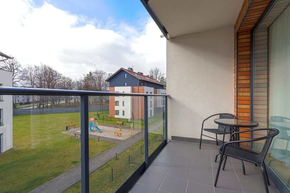 Sunny balcony with black table and two chairs, overlooking green courtyard and quiet surroundings.
