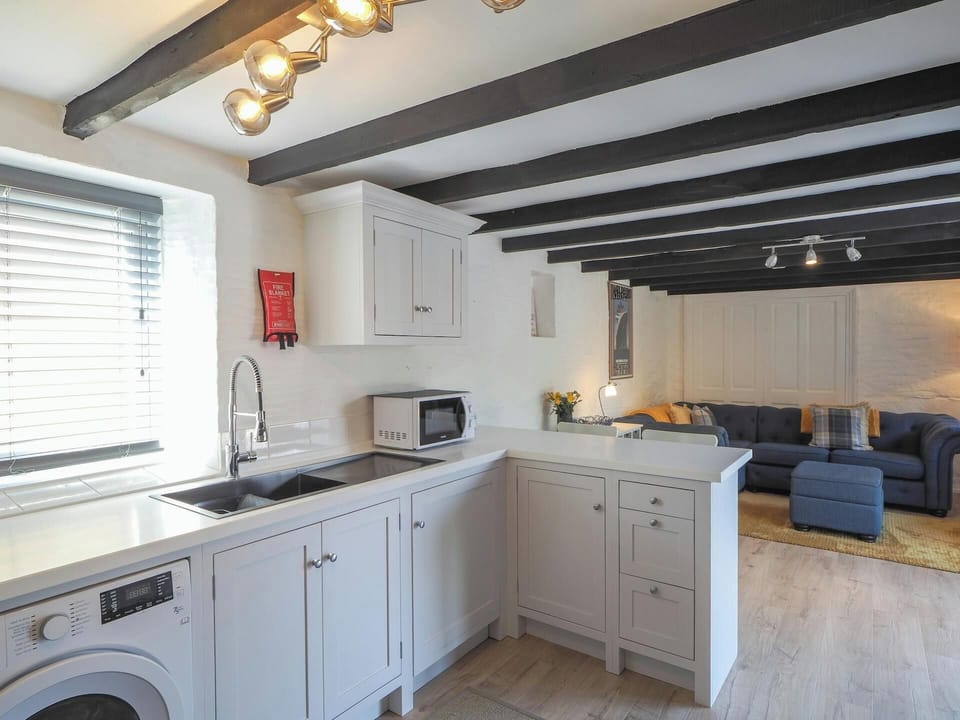 Kitchen area with washing machine, sink, microwave and sitting area in the background