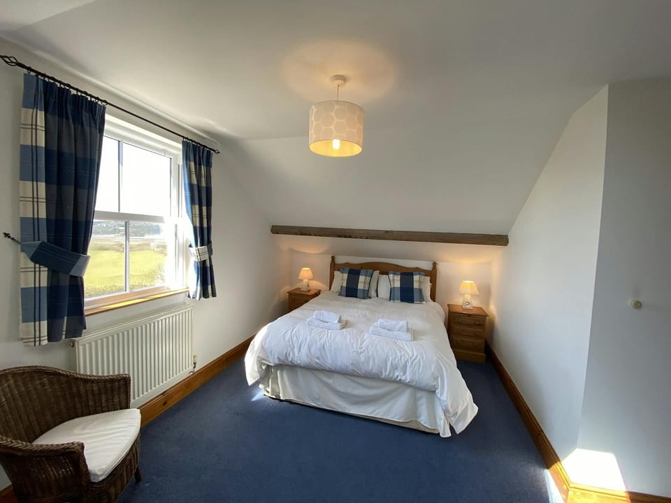Double bed, bedside drawers with lamps, wicker chair and radiator, window overlooking the coast