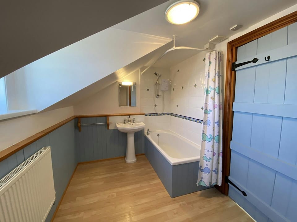 Bathroom with sloping ceiling, washbasin with mirror above, bath with shower over, radiator and window