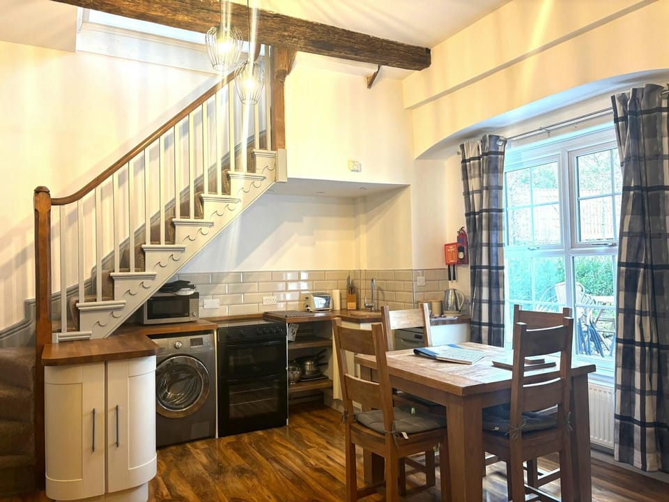 Open-plan kitchen diner with wooden table, stairs and large window with curtains