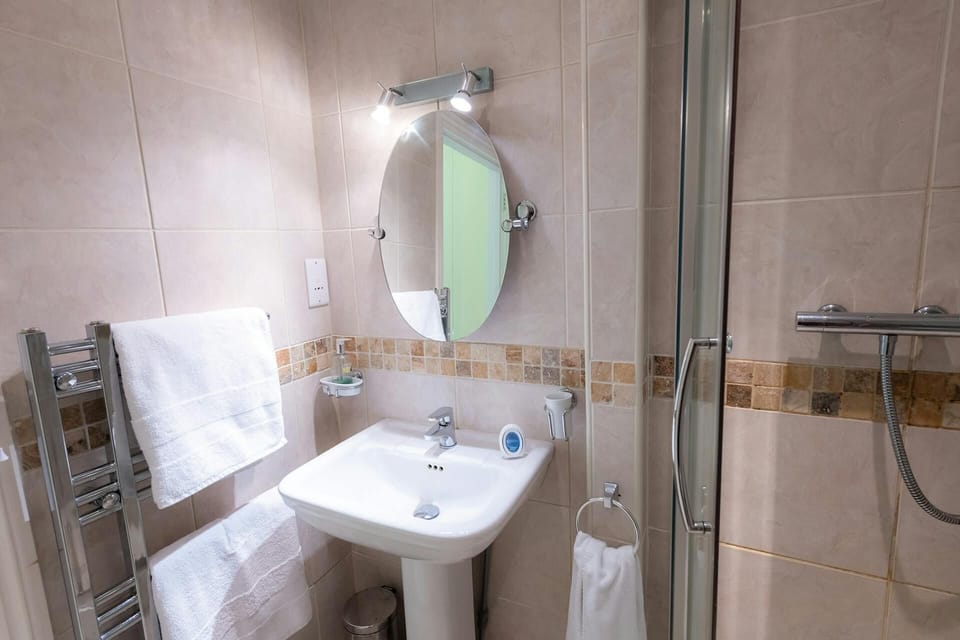 Bathroom with wash basin with wall mounted mirror and light above, shower cubicle and heated towel rail