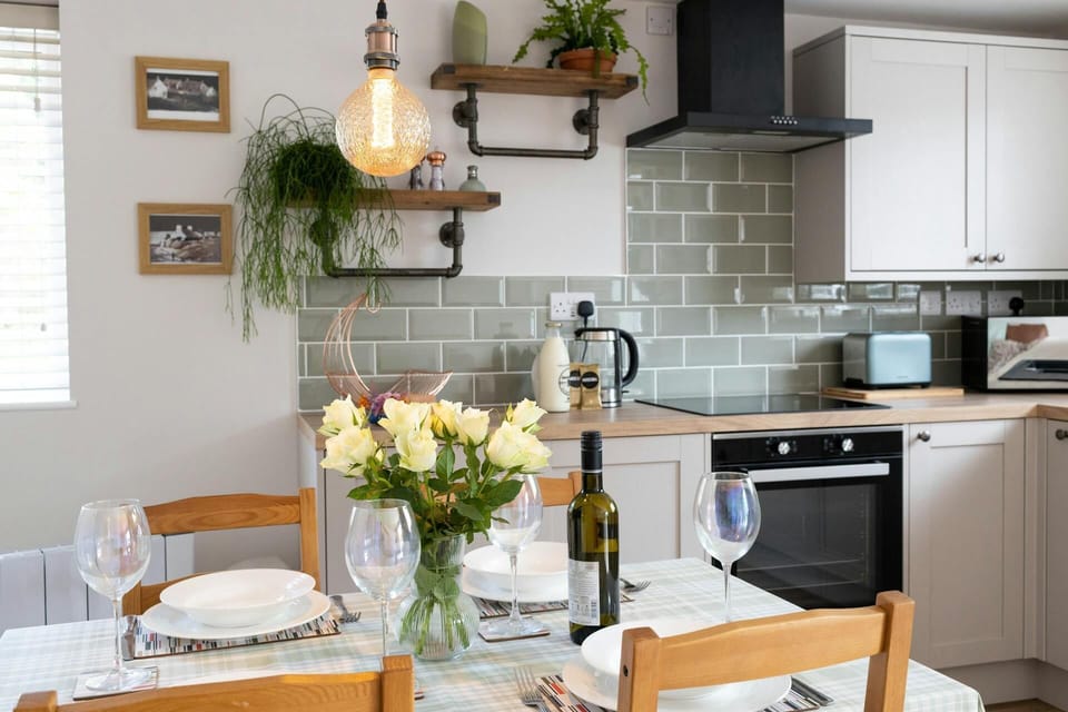 Dining table and chairs laid for lunch with a vase of flowers looking through to the kitchen