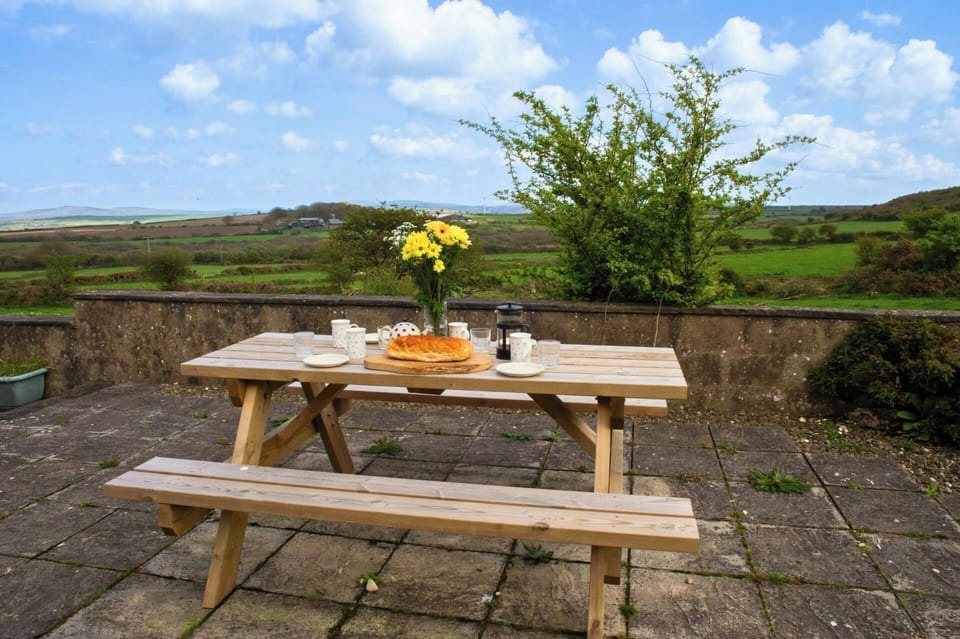 Wooden picnic table with bench on a stone patio, set with breakfast and flowers