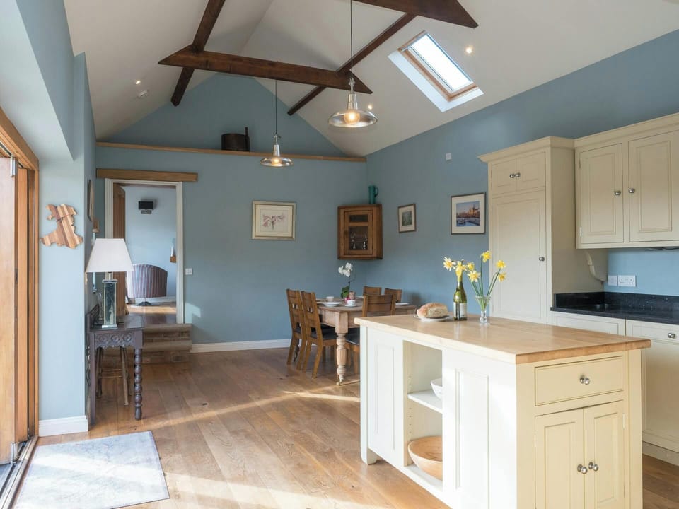 Open-plan kitchen diner with island, pale blue walls and wooden beams