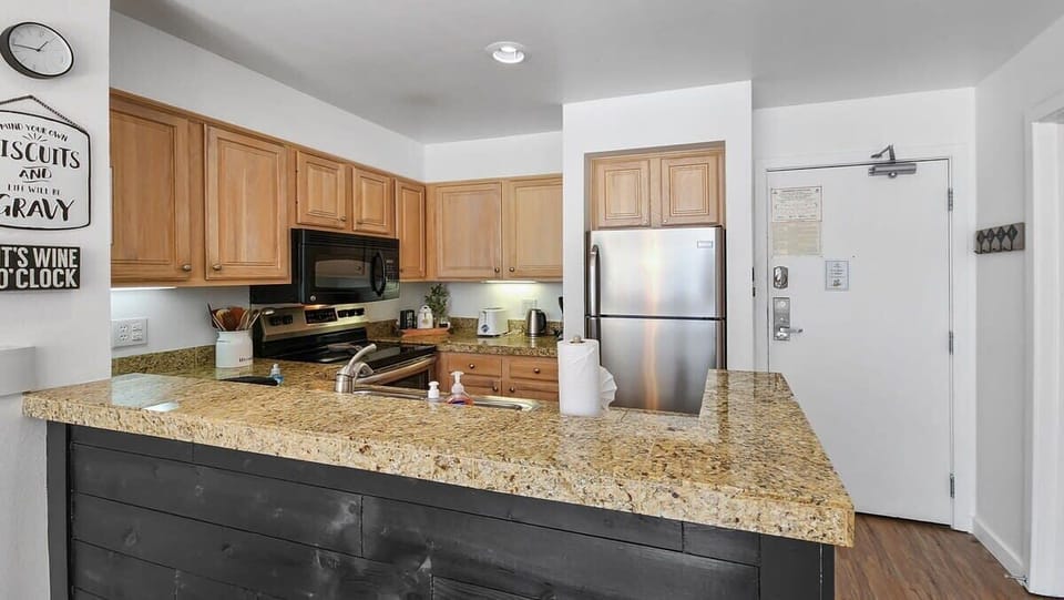 A well-kitchen is outfitted with stainless steel appliances, a range of cookware including an air fryer and crockpot, and a kitchen bar with seating for two.