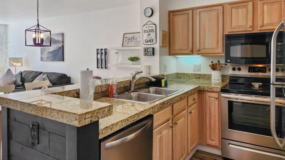 A well-kitchen is outfitted with stainless steel appliances, a range of cookware including an air fryer and crockpot, and a kitchen bar with seating for two.