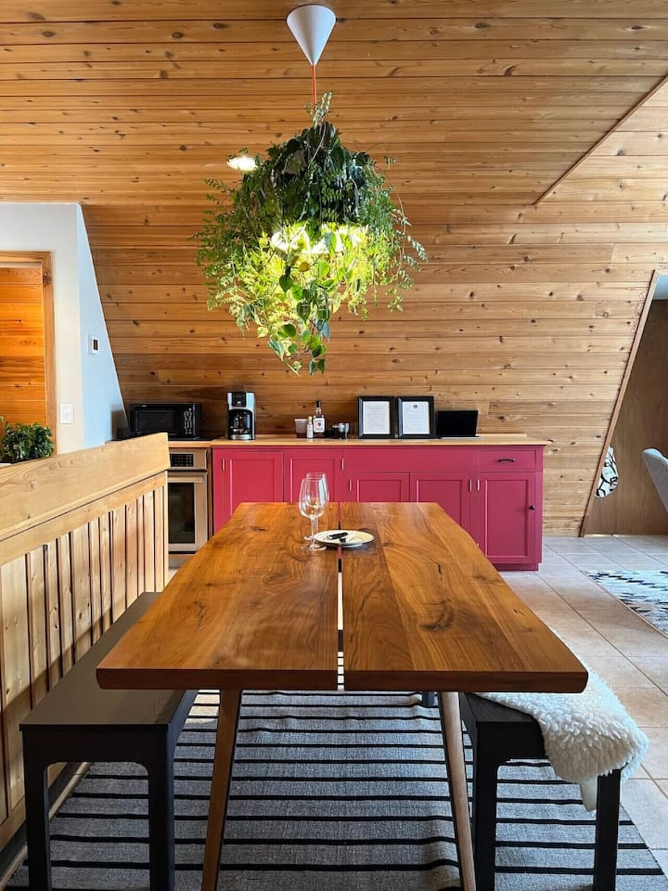 The live-edge A-Frame dining table with benches beneath the jungly planter light.