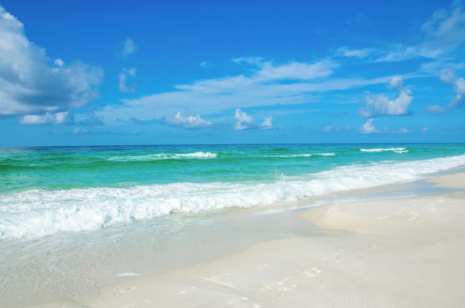 Just steps to the pristine white sand beach stretching along turquoise waters under brilliant blue skies with gentle waves rolling ashore.