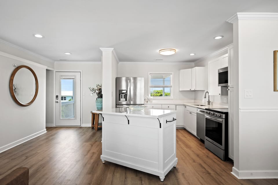 Step into a bright, coastal-inspired kitchen with stainless appliances, a charming center island, and glimpses of blue water just beyond the door.