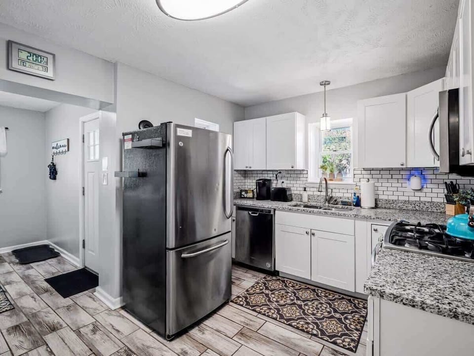 Bright, modern kitchen with crisp white cabinets, granite countertops, and subway tile backsplash. Stainless appliances and patterned wood-look floors flow seamlessly into the adjacent dining room for effortless entertaining! ️✨