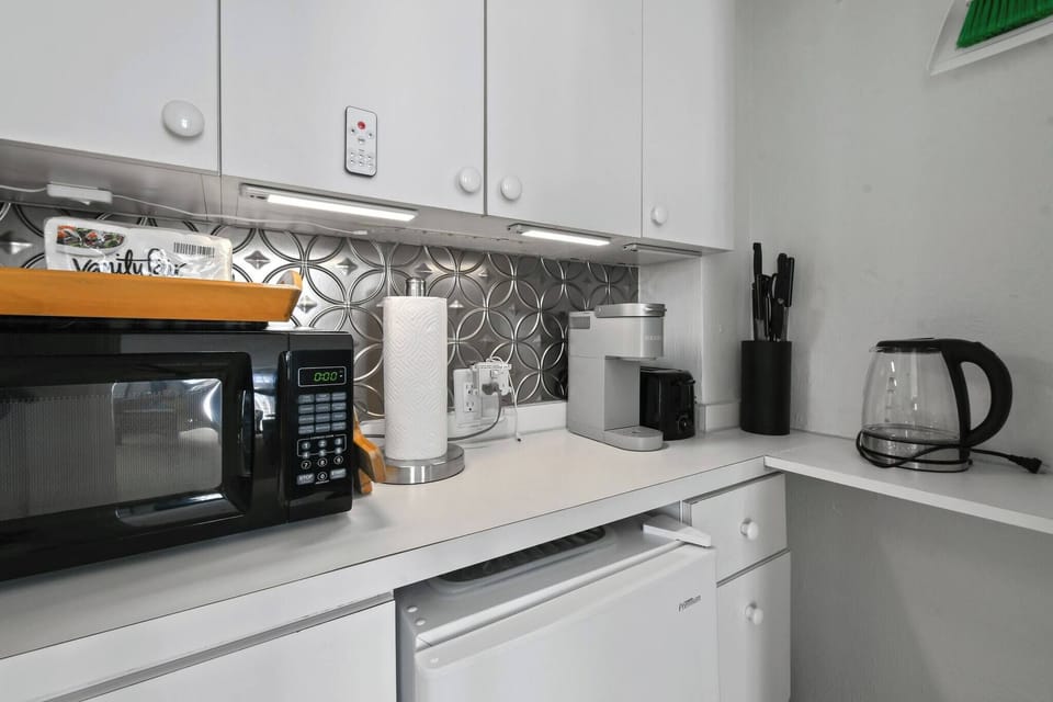 Kitchenette with microwave, toaster, mini fridge, Keurig coffee maker, glasses, plates, and cutlery. No Sink