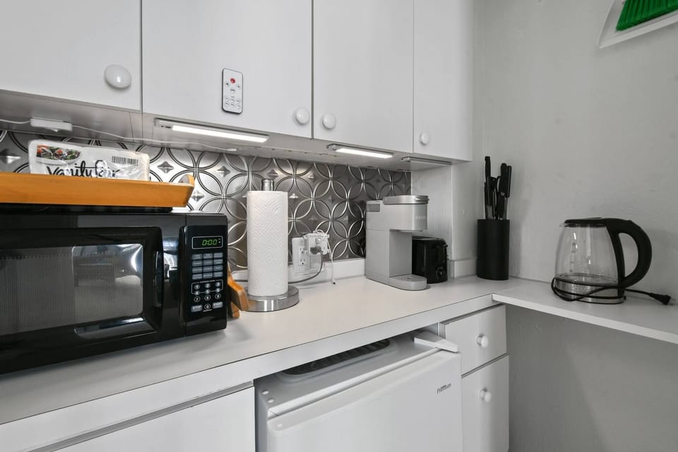 Kitchenette with microwave, toaster, mini fridge, Keurig coffee maker, glasses, plates, and cutlery. No Sink
