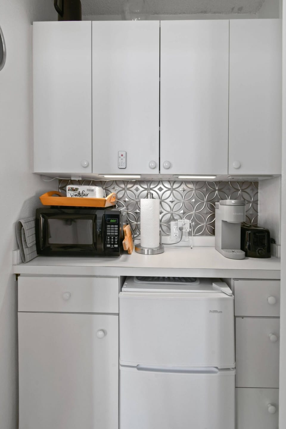 Kitchenette with microwave, toaster, mini fridge, Keurig coffee maker, glasses, plates, and cutlery. No Sink