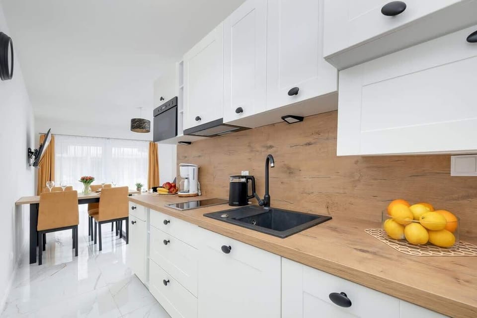 A full view of the kitchen and adjacent dining area, showing the layout. The dining table is small and cozy, with two chairs, and the kitchen continues with a modern white-and-wood theme.