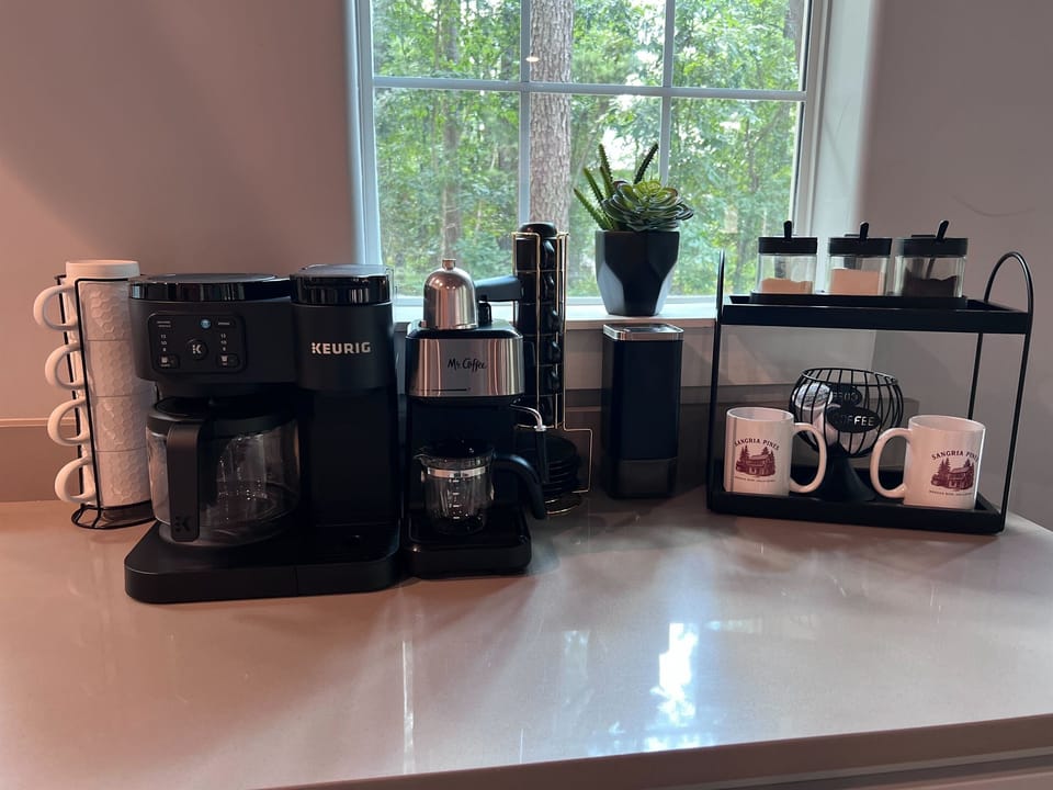 COFFEE BAR | Fully stocked coffee station featuring Keurig and Mr. Coffee machines, assorted mugs, and a variety of sweeteners for guest convenience.