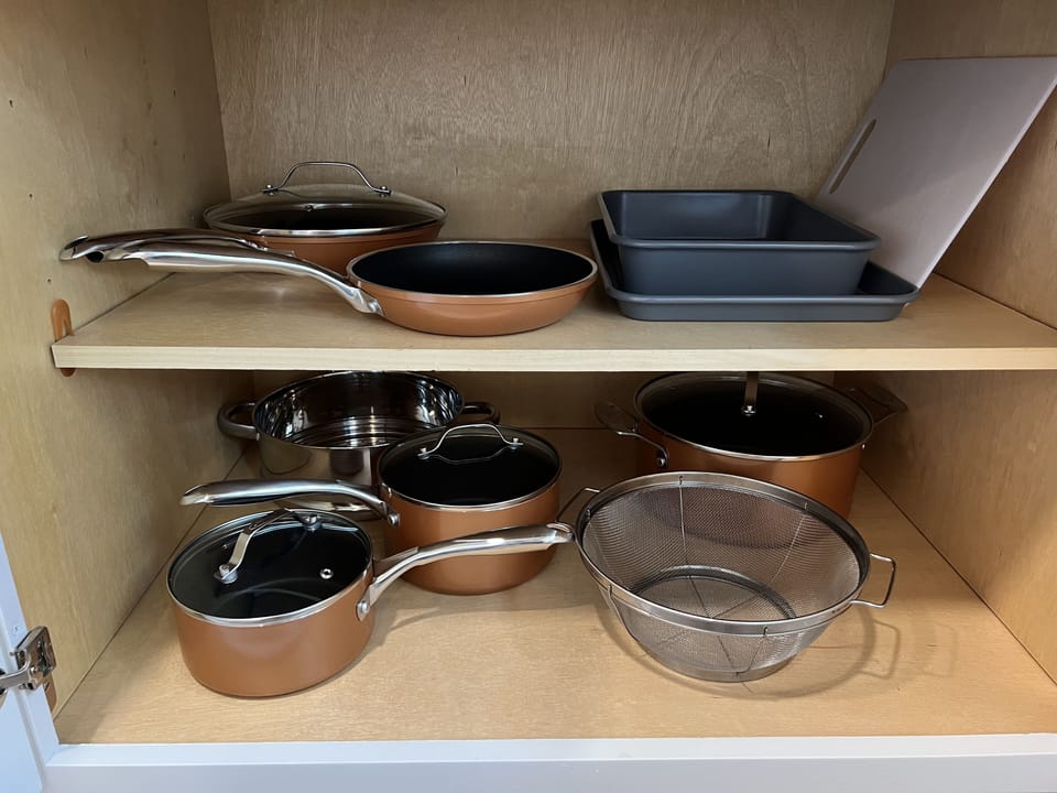 Pots, pans, colanders, baking trays, and cutting board in kitchen