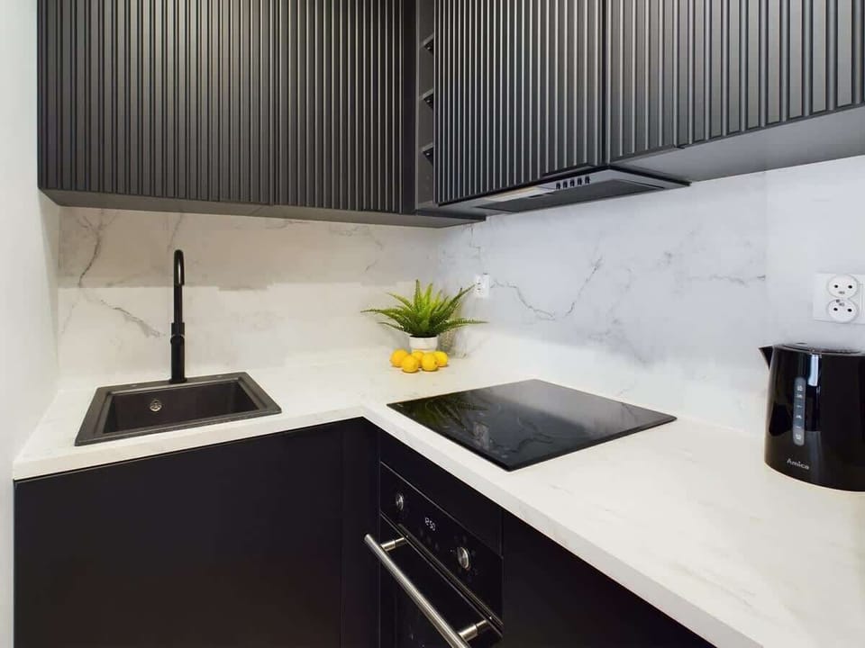 A close-up of a kitchen sink with dark cabinets and a white countertop. The space is clean and modern.