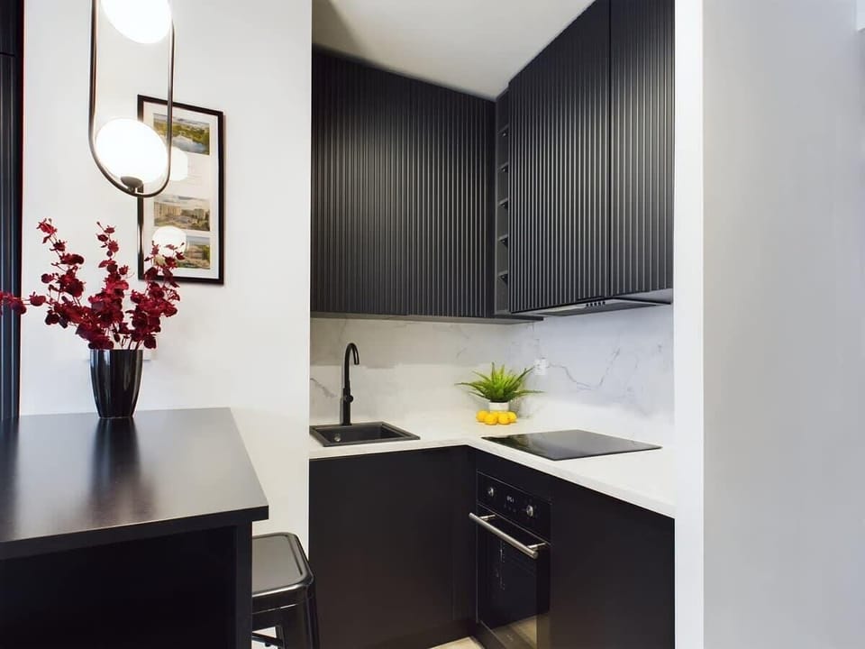 A dark-colored kitchen area with cabinets and a sink. A vase with flowers is on the counter.