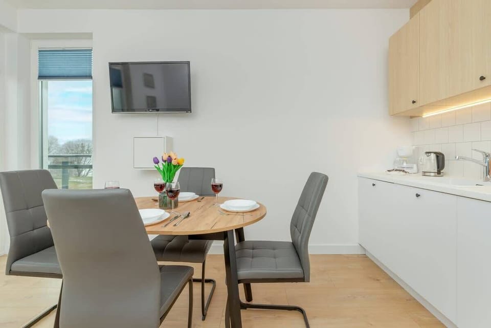 A dining area features a wooden table with chairs, under a modern pendant light, with a window view.