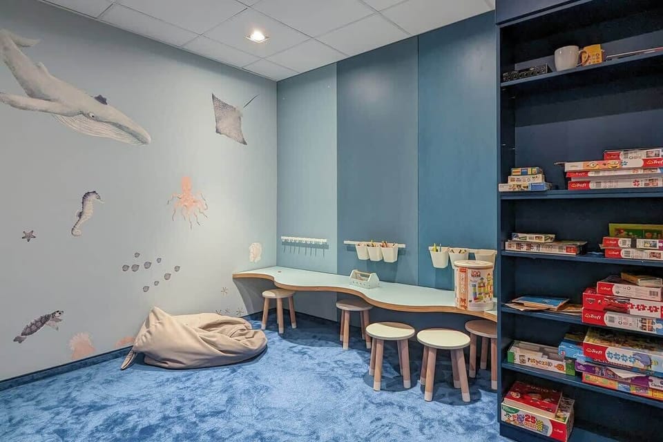 The blue playroom, with a nautical theme on the walls, offers a creative space for children, equipped with a drawing table and shelves of games.