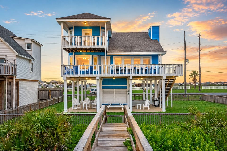 Bright blue raised beach house exterior with front stairs, fenced yard area, elevated deck, and coastal curb appeal near San Luis Pass in Galveston.
