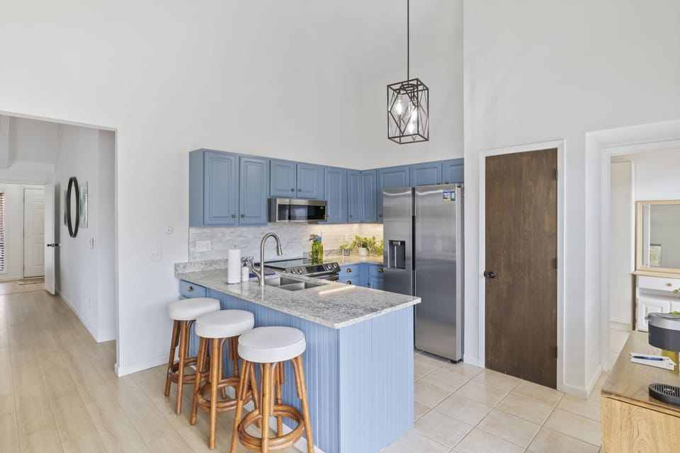This fully equipped kitchen features stainless steel appliances, beautiful blue cabinetry, and a granite countertop breakfast bar with seating for three.