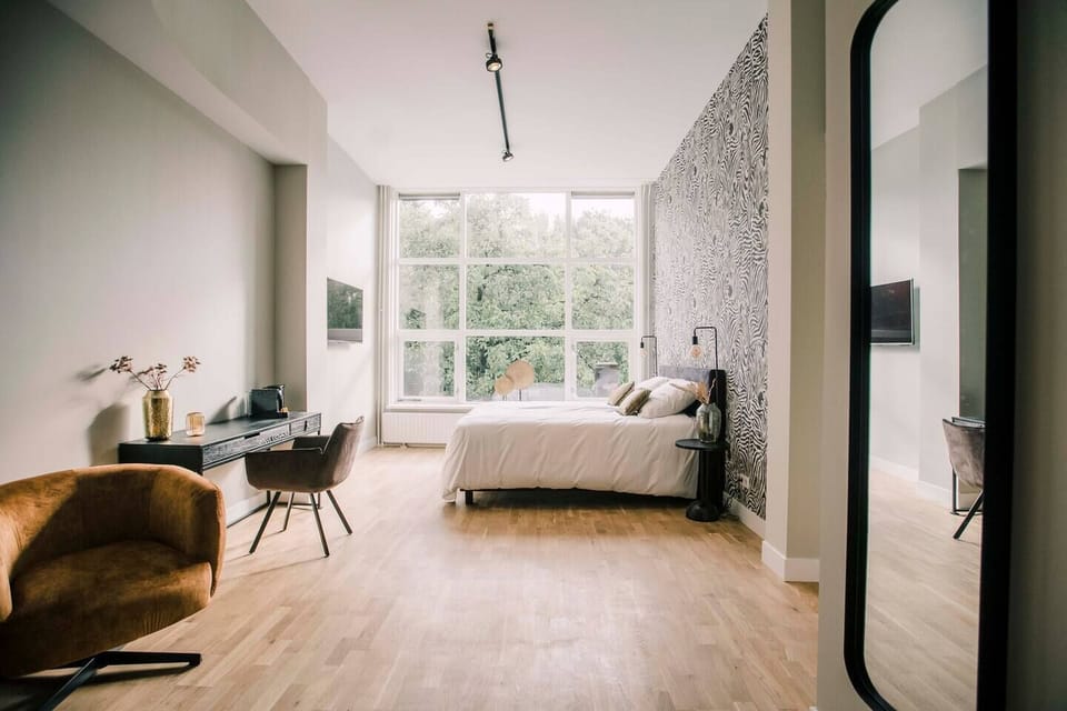 A spacious, modern bedroom with floor-to-ceiling windows, zebra-print accent wall, cozy furnishings, a sleek desk, and warm lighting for a serene atmosphere.