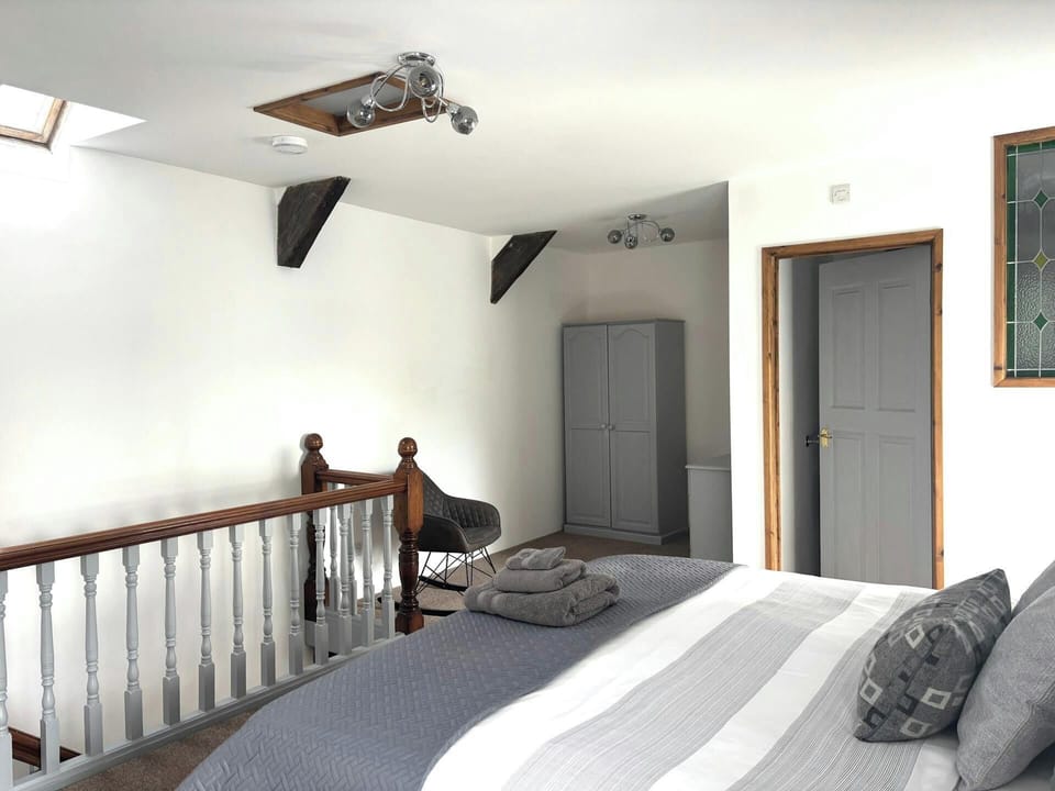 Double bed with grey bedding beside wooden staircase railing