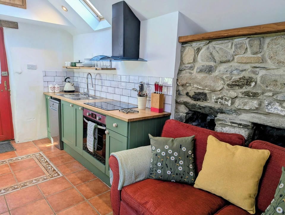 Open-plan kitchen with green units, tiled splashback and terracotta floor tiles