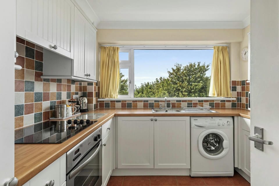 Kitchen with white cabinets, cooker, microwave and washing machine under the counter