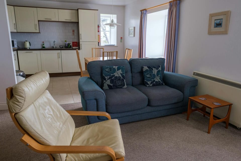 Lounge area with sofa, armchair and coffee table leading to the fitted kitchen