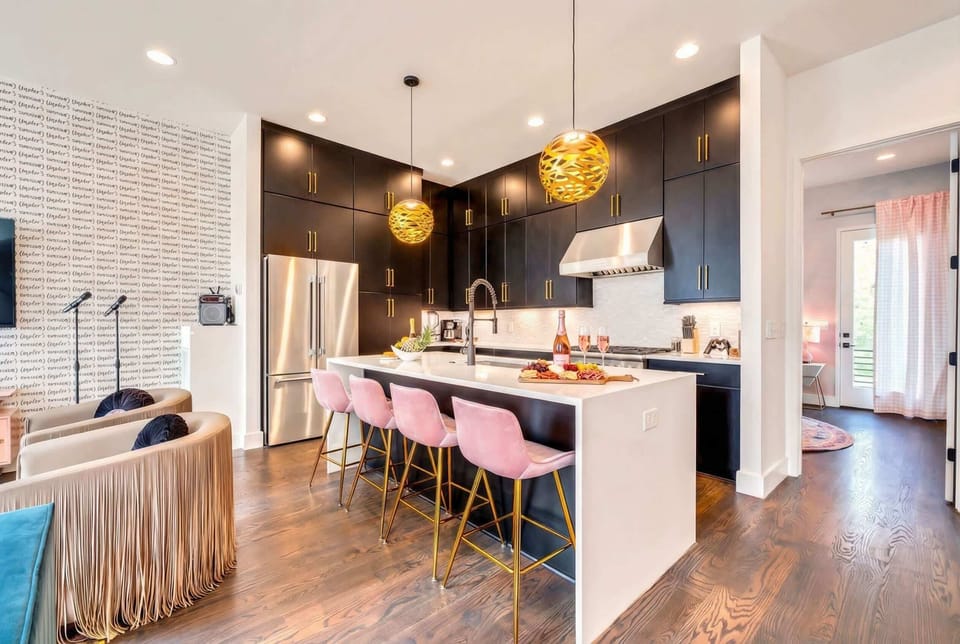 Black kitchen cabinets, white island with pink bar stools, and gold pendant lights make this the coolest kitchen in the neighborhood for group cooking