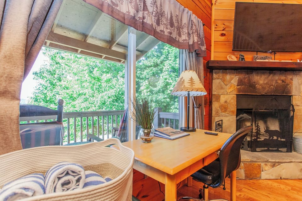 Screened porch seating area with wicker furniture and a stone fireplace overlooking mountain scenery near Bryson City. Covered outdoor living space designed for enjoying Smoky Mountain views.