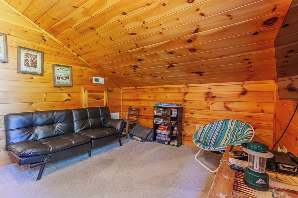 Loft seating area with leather futon, wood-paneled walls, and open layout. Relaxing indoor gathering space inside this Bryson City mountain cabin.