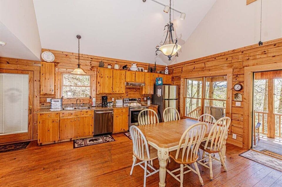 Dining area with wood table and chairs adjacent to the kitchen and exterior access doors. Vaulted ceilings and wood finishes enhance the mountain cabin character.