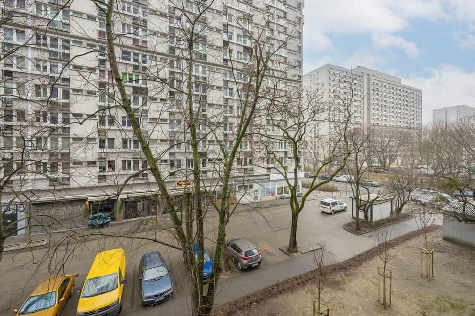 A city view from the apartment, showcasing residential buildings and parked cars on the street below.

